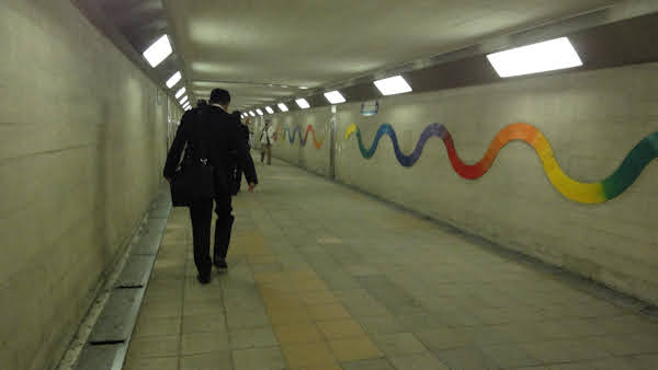 a drab underground walkway with a wavy multicoloured line decorating one wall